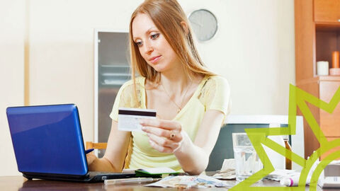 Junge Frau sitzt mit ihrer EC Karte vor dem Laptop