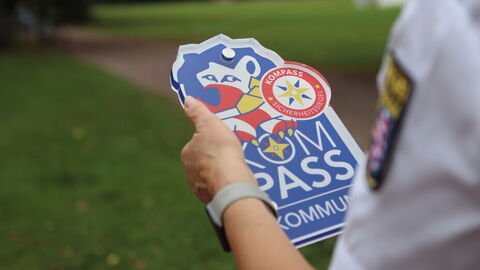 KOMPASS-Schild in den Händen einer Polizeibeamtin