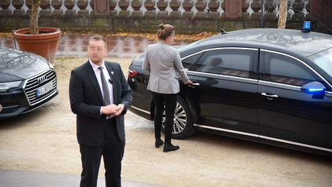 Der Personenschutz steht am Fahrzeut, eine Personenschützin ist dabei die Fahrzeugtür zu öffnen